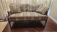 Front view of one antique French settee showing wooden frame, patterned upholstery, and down cushions.