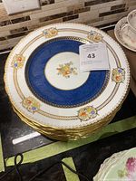 Stack of 12 Aynsley plates showing cobalt blue band with gold and floral detailing.