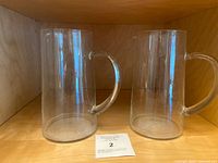 Two clear glass pitchers displayed side by side on a wooden shelf, showing their shape and clarity.