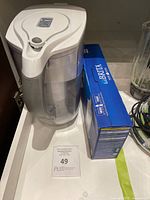 White Brita water filter pitcher next to a box of replacement Brita water filters on a shelf.