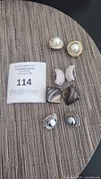 Overview photo of all four pairs of clip-on earrings arranged on woven surface showing various shapes and designs including pearl, rhinestones, silver squares, and gray pearl-like earrings.