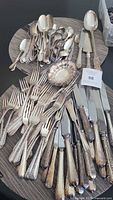 Photo showing assorted knives, forks, and spoons with ornate silver-colored handles on a wooden tray.