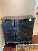 Front view of the black French commode showing four curved drawers with gold floral detailing and ring pull handles.