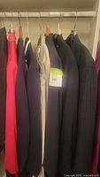 Side view of multiple jackets and suits on hangers showing color variety including red, black, beige, and pinstripe
