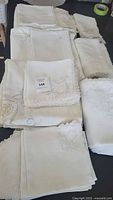 Collection of assorted white and off-white linens with lace edging and hand embroidery, laid out on a dark surface.