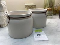 Pair of white ceramic planter pots with brown rim and cord bows on a countertop, accompanied by a lot number card