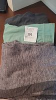 Three folded pairs of Lululemon pants stacked showing dark gray, mint green, and heathered gray colors with tag number 192.