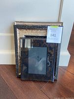 Three stacked decorative frames leaning against a wall on hardwood floor, showing front sides