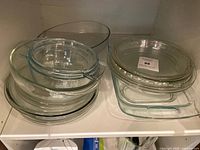 Clear glass Pyrex cookware including bowls, baking and casserole dishes, arranged on a white shelf.