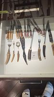 Drawer with a variety of cutting utensils and some serving cutlery all featuring natural antler handles. Visible wood drawer sides and measuring tape for scale above.