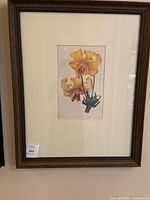 Framed print of yellow-orange lilies signed by Paxton, showing the full artwork, matting, and brown wooden frame with decorative beading.
