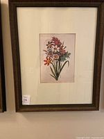 Framed signed floral print featuring multiple flower types in red, purple, white, and orange tones with green leaves. Mounted on cream mat in dark carved wooden frame.