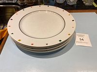 Stack of four white fine china dinner plates with thin black inner circle and multicolored geometric shapes around the rim