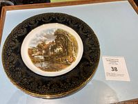 Photo showing a rare antique Aynsley fine bone china plate with an intricate countryside scene in the center, ornate gold pattern on a dark blue rim, and 22K gold edging.