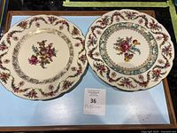 Two vintage decorative china plates side by side on a table, showing floral and gold decorative patterns.