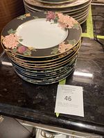 Stack of 10 Fitz & Floyd decorative plates featuring cloisonné peony black pattern on black background with gold trim, placed on kitchen countertop.