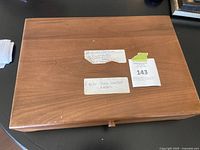 Closed wooden case with labels indicating the contents of Rogers silverware including bread butter knives, dessert knives, cheese knife, soup spoons, and miscellaneous bone handle knives.