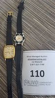 Two wristwatches displayed side by side on a woven mat with auction lot number card visible