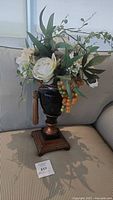 Front view of the black and copper decorative vase with silk artificial flowers and faux berry arrangement on a striped couch.