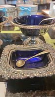 Close-up of square silver plated cellar with cobalt blue glass liner and silver spoon resting inside.