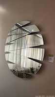 Front view of the silver segmented rhythm mirror showing the fragmented oval pattern and reflection of curtains and couch.