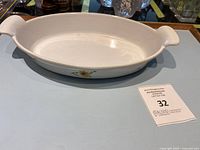 Oval Descoware cast iron enamel au gratin pan with white floral design and dual handles on a blue surface.