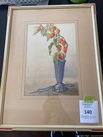 Framed floral print featuring orange lantern-like flowers in a blue vase, with a blue beaded necklace on the table.