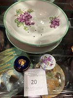 Photo of colander with purple grape pattern along with two porcelain trinket boxes, one cobalt blue with gold and one white with floral design