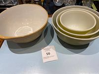 Photo of a set of 4 mixing bowls on a blue surface, including 3 nested green and white Pyrex bowls and 1 larger cream ceramic bowl with yellow rim.