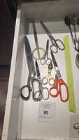 Top-down view inside drawer showing seven pairs of scissors including Hoffritz sewing shears with various handle styles and sizes.