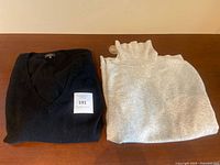 Two sweaters folded on a wooden surface, one black V-neck and one light gray turtleneck.