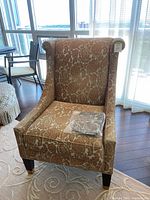 Front angle of large wingback reading chair with floral velvet fabric, dark tapered legs with brass feet caps, located in a room with wood floors and glass windows.