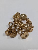 Close-up photo of a pile of small 10K gold earring backs, showing their shape and design.
