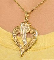 Pendant hanging and worn around a neck showing detailed design and luster of the gold and diamonds.