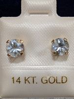 Front view of two aquamarine stud earrings in 14K gold prong setting displayed on a white satin holder.