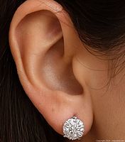 Close-up image of one earring worn on an ear showing 14K gold stud with round faceted clear moissanite gemstone.