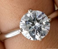 Close-up front view of the round faceted moissanite stone on a silver-colored band ring, showing clarity and cut details.