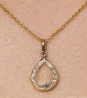 Close-up of pendant worn on skin showing teardrop-shaped transparent lab diamond in 10K gold setting.