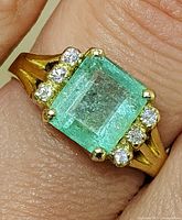 Close-up front view of ring on finger showing emerald and diamond accents