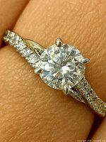 Ring on finger close-up showing round center moissanite and pavé shoulders.