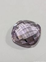 Checkerboard faceted cushion cut light purple amethyst gemstone on white background.