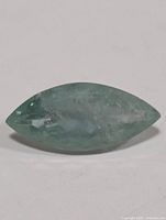 Close-up of an elongated marquise cut light blue-green aquamarine gemstone showing surface and internal inclusions