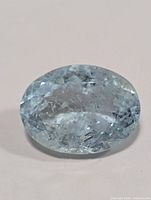 Top view of an oval light blue faceted aquamarine gemstone showing inclusions and cut facets.
