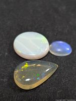 Three genuine Australian opal stones on black background: white oval, blue oval, and yellow teardrop shape.