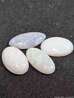 Four oval white Australian opal cabochon gemstones on dark background showing play-of-color.