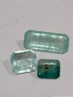 Three Colombian emeralds laid on white surface showing size and color differences.