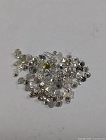 Close-up of multiple small loose diamonds on white surface showing various shapes and sizes with slight color variations.