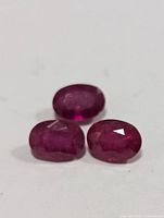 Three oval-shaped genuine enhanced rubies of deep red color with faceted cuts and visible inclusions.