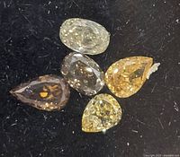Close-up of five loose fancy color diamonds in various shapes and colors on a black background.