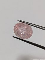 Close-up of pink oval cut morganite gemstone held with tweezers showing clarity and faceting details